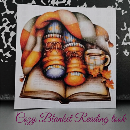 Cozy fall sticker with boots, socks, plaid blanket, open book and coffee mug